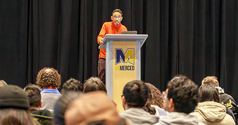 Males at podium lecturing to group of students